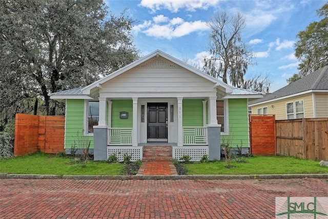 bungalow-style home with covered porch, fence, a front lawn, and metal roof