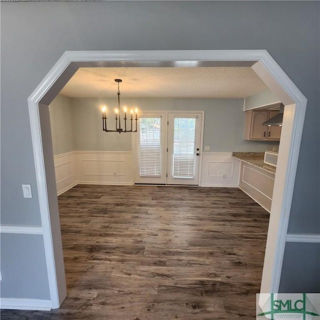 unfurnished dining area with a decorative wall, a notable chandelier, dark wood-style flooring, and wainscoting