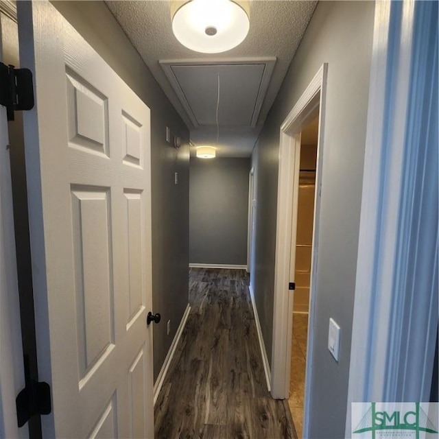 hall with a textured ceiling, attic access, baseboards, and wood finished floors