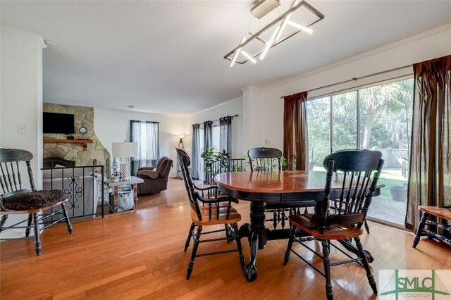 dining space with light wood-style floors, crown molding, and a stone fireplace