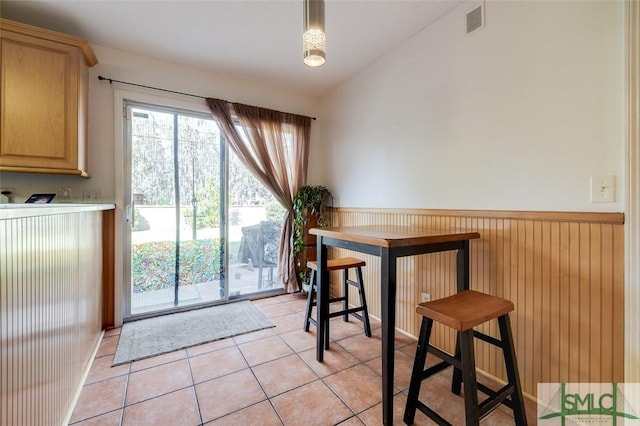 dining area featuring light tile patterned floors, visible vents, vaulted ceiling, and wainscoting