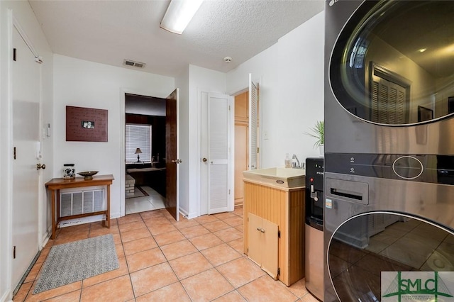 kitchen with light tile patterned floors, oven, a sink, visible vents, and stacked washing maching and dryer