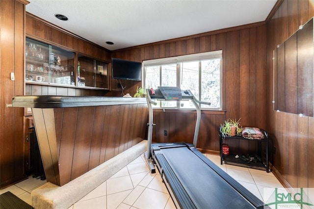 exercise area with light tile patterned flooring, wood walls, and a bar