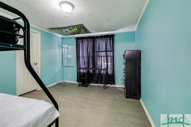 bedroom featuring a textured ceiling, ornamental molding, wood finished floors, and baseboards