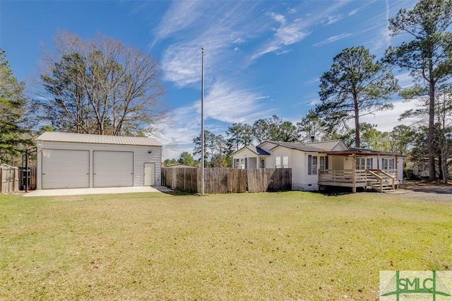 exterior space featuring a wooden deck, a detached garage, fence, and an outbuilding