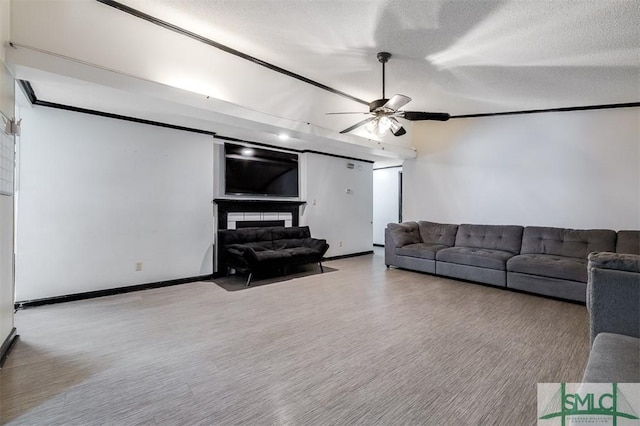 living area featuring a textured ceiling, ceiling fan, baseboards, a glass covered fireplace, and crown molding