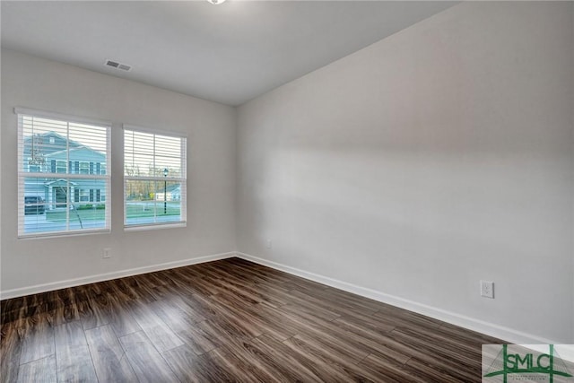 empty room with dark wood-type flooring, visible vents, and baseboards