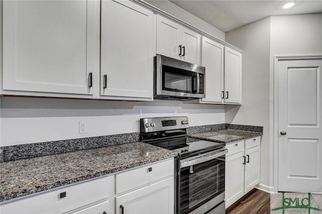 kitchen featuring white cabinets, dark wood-style floors, appliances with stainless steel finishes, dark stone countertops, and recessed lighting