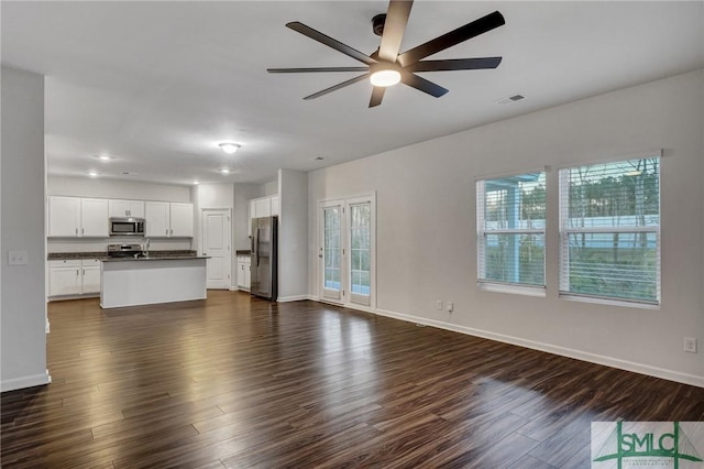 unfurnished living room with dark wood-type flooring, visible vents, baseboards, and a ceiling fan