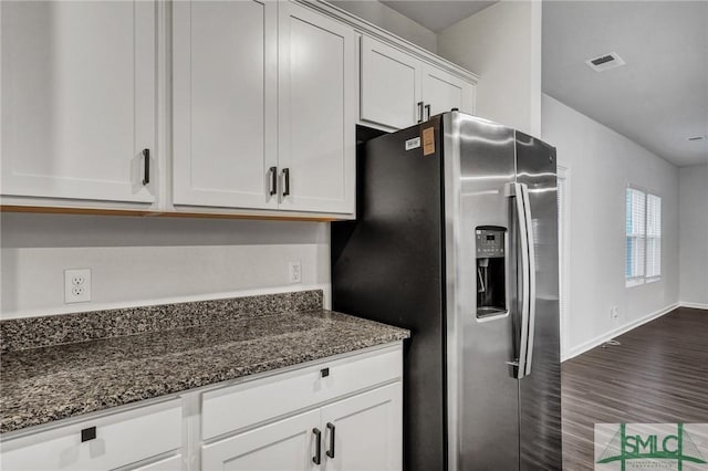 kitchen with stainless steel refrigerator with ice dispenser, visible vents, dark wood-type flooring, white cabinetry, and dark stone countertops