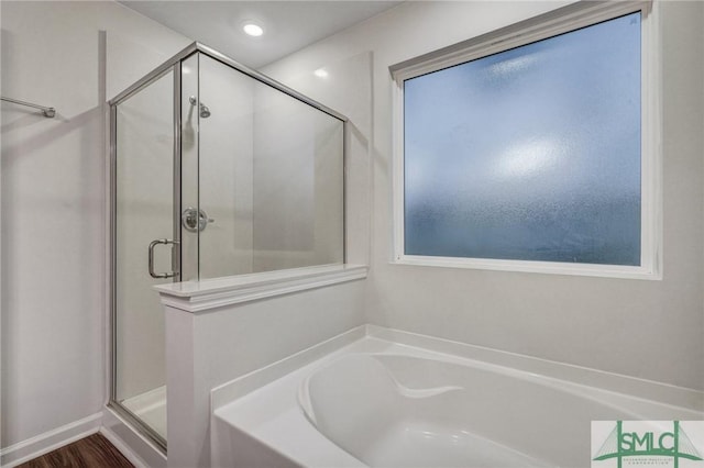 bathroom with a stall shower, a bath, and wood finished floors