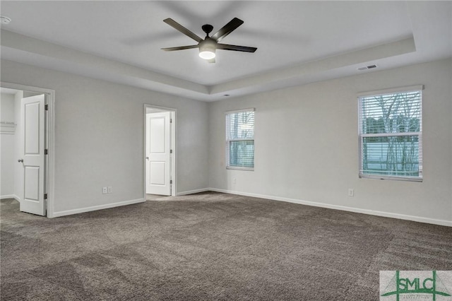 spare room featuring baseboards, visible vents, a ceiling fan, a raised ceiling, and dark colored carpet