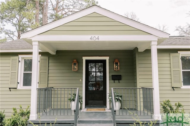 doorway to property with covered porch and a shingled roof