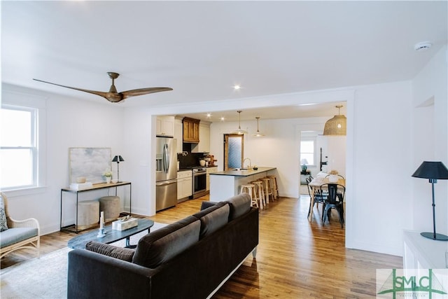 living area with light wood-style flooring, baseboards, a ceiling fan, and recessed lighting