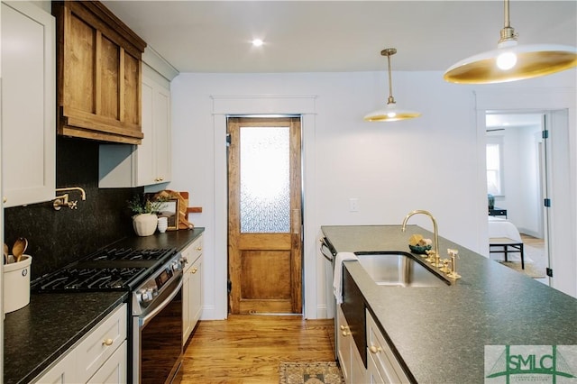 kitchen with tasteful backsplash, light wood-type flooring, stainless steel range with gas stovetop, a healthy amount of sunlight, and a sink