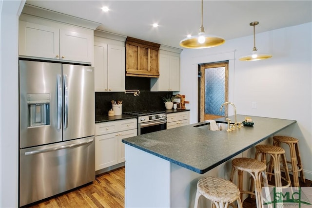 kitchen featuring a breakfast bar area, stainless steel appliances, a sink, decorative backsplash, and dark countertops