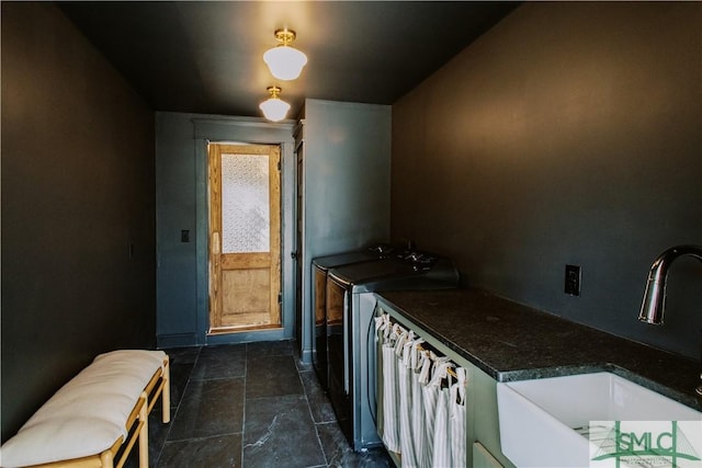 kitchen with separate washer and dryer, dark countertops, a sink, and stone tile floors