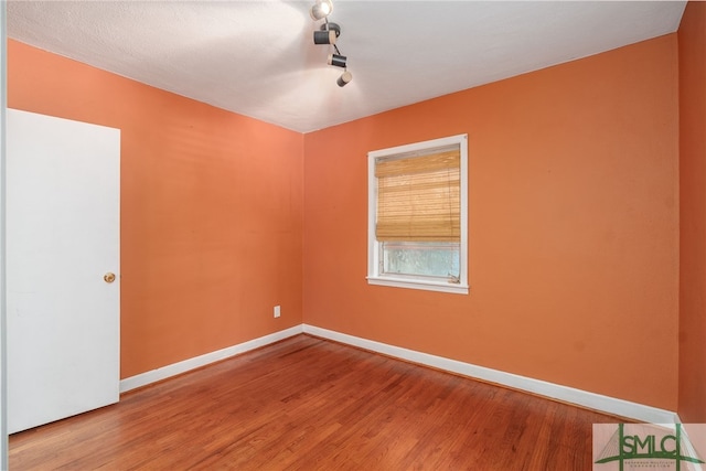 empty room with track lighting, baseboards, and wood finished floors