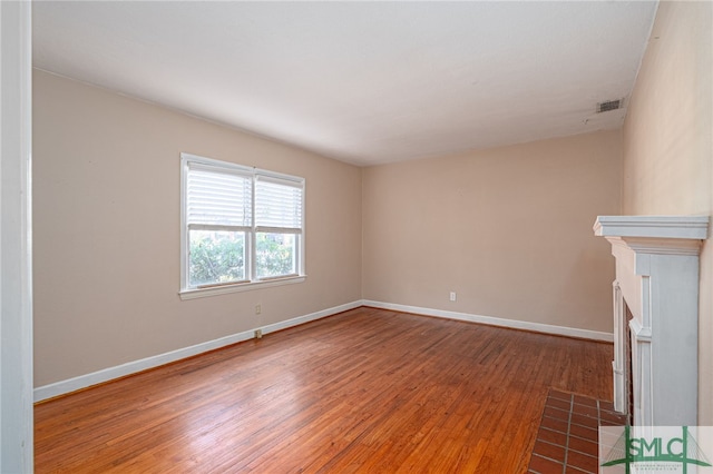 unfurnished living room featuring a fireplace with flush hearth, wood finished floors, visible vents, and baseboards