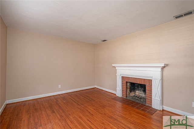 unfurnished living room with hardwood / wood-style flooring, a fireplace, visible vents, and baseboards