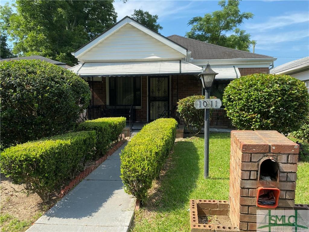 bungalow-style home with a shingled roof, a front yard, covered porch, and brick siding