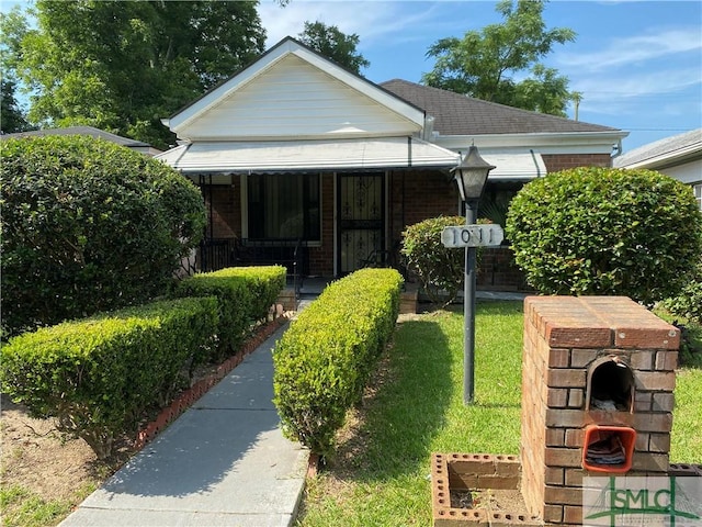 bungalow-style home with a shingled roof, a front yard, covered porch, and brick siding