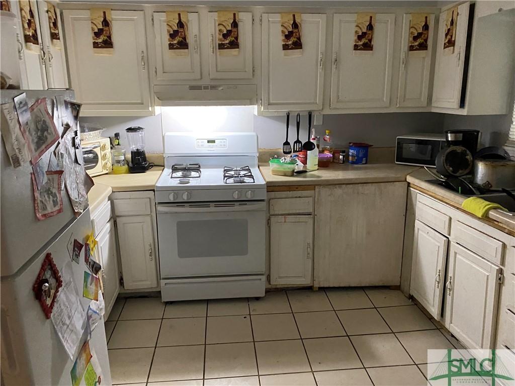 kitchen with white appliances, light countertops, under cabinet range hood, and light tile patterned flooring