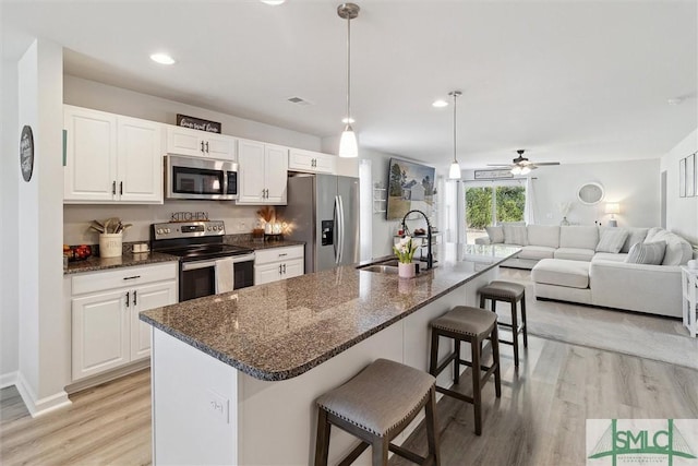 kitchen featuring a breakfast bar area, light wood-style flooring, stainless steel appliances, a sink, and white cabinetry