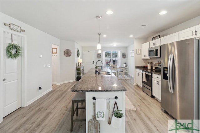 kitchen with stainless steel appliances, visible vents, white cabinetry, a sink, and a kitchen bar