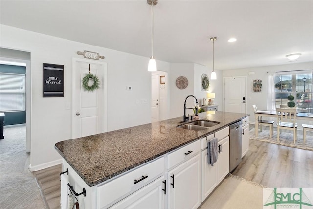 kitchen featuring a sink, light wood-style floors, white cabinets, stainless steel dishwasher, and dark stone countertops