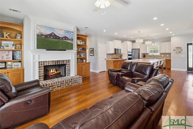 living area featuring recessed lighting, dark wood-type flooring, visible vents, baseboards, and a brick fireplace