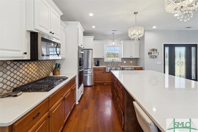 kitchen with a notable chandelier, stainless steel appliances, a sink, white cabinets, and dark wood-style floors