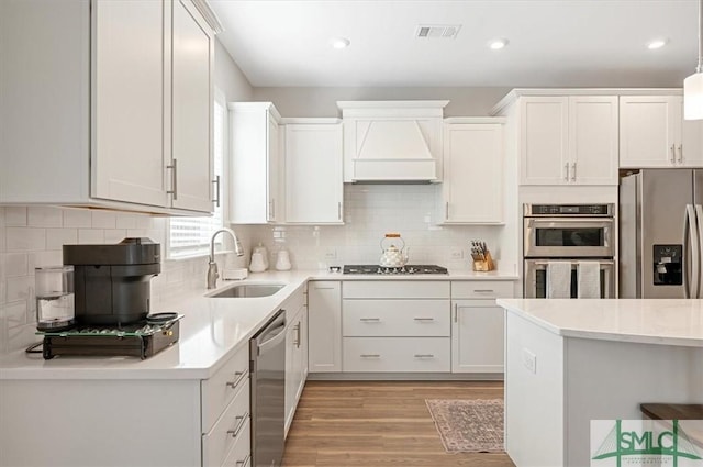 kitchen featuring light wood finished floors, visible vents, custom exhaust hood, stainless steel appliances, and a sink