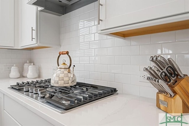 kitchen with tasteful backsplash, white cabinets, light stone counters, under cabinet range hood, and stainless steel gas stovetop