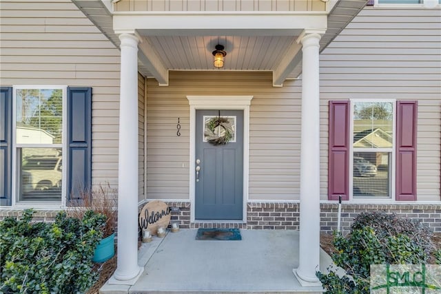 view of exterior entry featuring a porch and brick siding