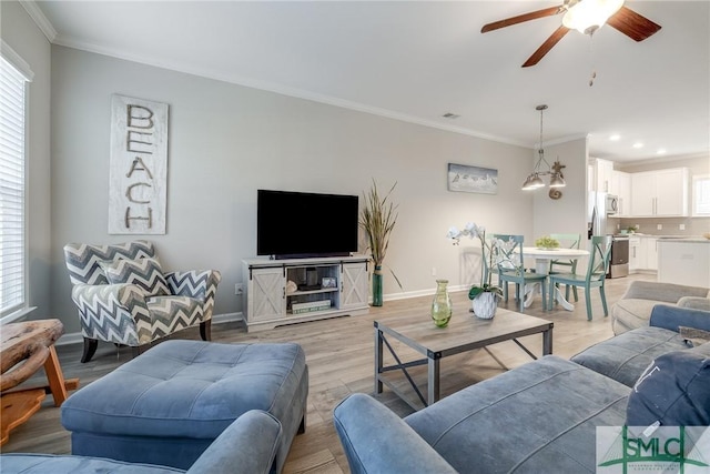 living area featuring a healthy amount of sunlight, light wood-type flooring, baseboards, and crown molding