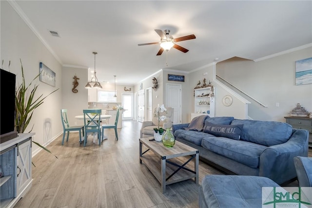 living room featuring light wood finished floors, visible vents, baseboards, a ceiling fan, and ornamental molding