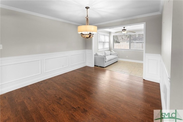 unfurnished dining area featuring wainscoting, crown molding, a ceiling fan, and wood finished floors