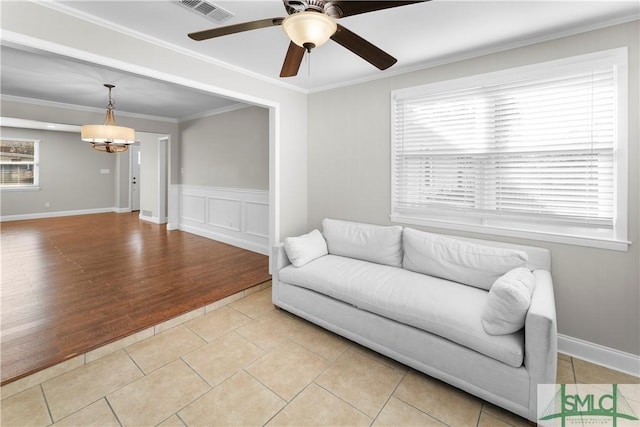 sitting room with visible vents, ceiling fan, ornamental molding, tile patterned floors, and a decorative wall