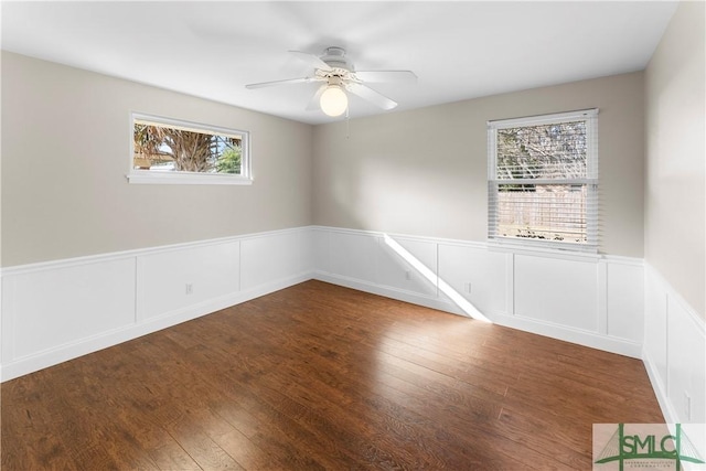 unfurnished room with a ceiling fan, wood-type flooring, and wainscoting