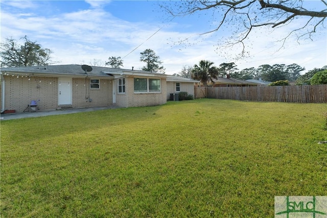 rear view of house with central AC unit, a yard, fence, and brick siding