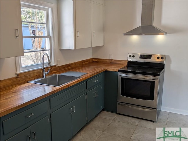 kitchen with a wealth of natural light, a sink, stainless steel electric range, wall chimney exhaust hood, and butcher block counters