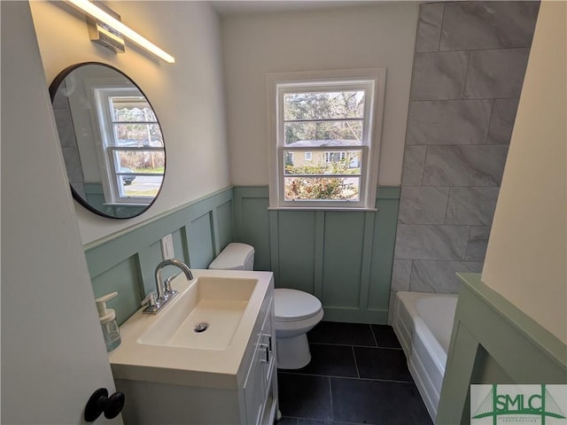 full bathroom with tile patterned floors, a wainscoted wall, toilet, a tub, and vanity