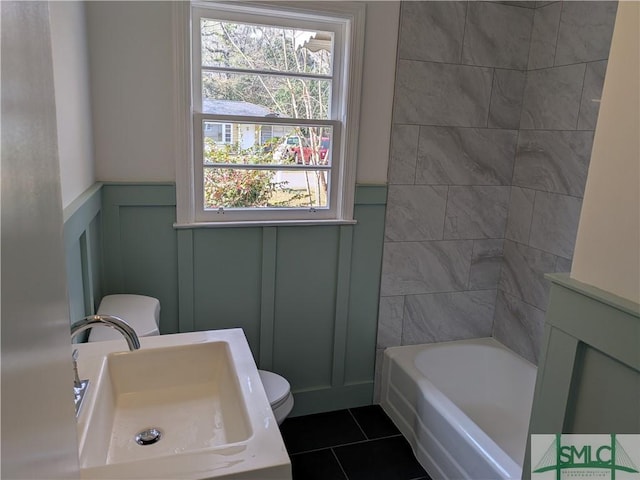 bathroom featuring a wainscoted wall, toilet, tile patterned floors, a decorative wall, and a sink