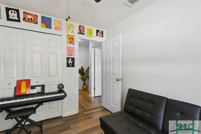 sitting room with visible vents, baseboards, a textured ceiling, and wood finished floors