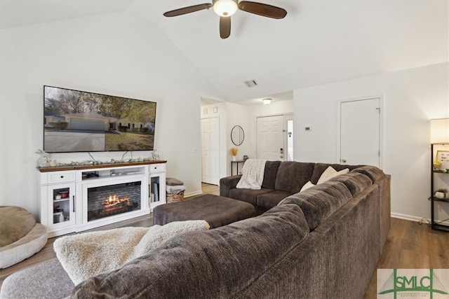 living area featuring visible vents, wood finished floors, a lit fireplace, lofted ceiling, and ceiling fan