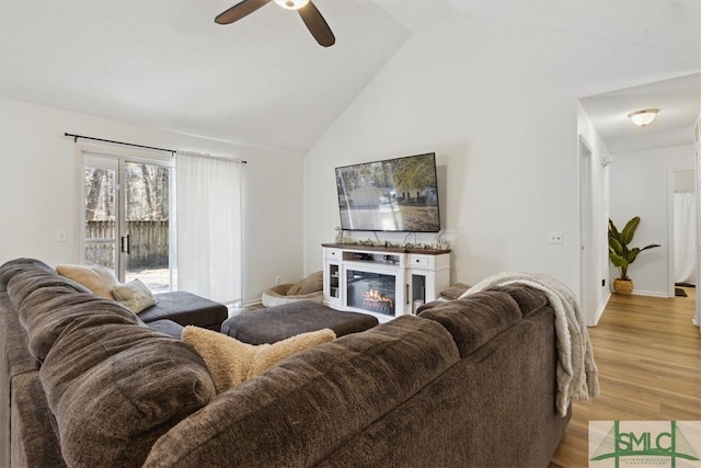 living room with a glass covered fireplace, light wood-type flooring, a ceiling fan, and vaulted ceiling