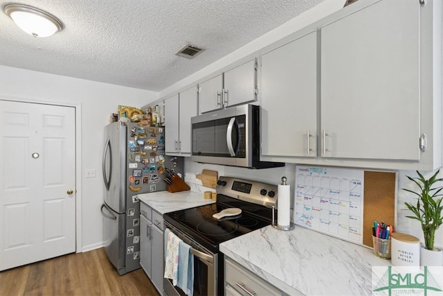 kitchen featuring light stone counters, wood finished floors, visible vents, stainless steel appliances, and a textured ceiling