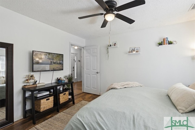 bedroom featuring visible vents, baseboards, ceiling fan, wood finished floors, and a textured ceiling