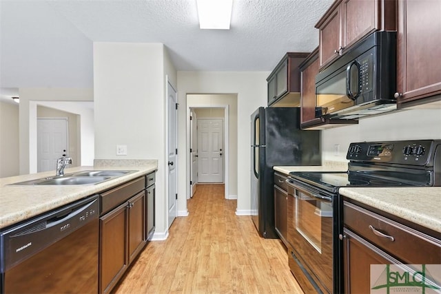 kitchen featuring light wood-style flooring, a sink, black appliances, light countertops, and a textured ceiling